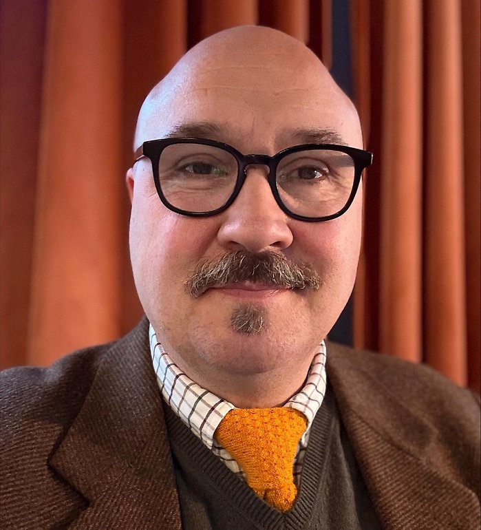 Bild på Johan Nicander. Han har glasögon och en brun kavaj.