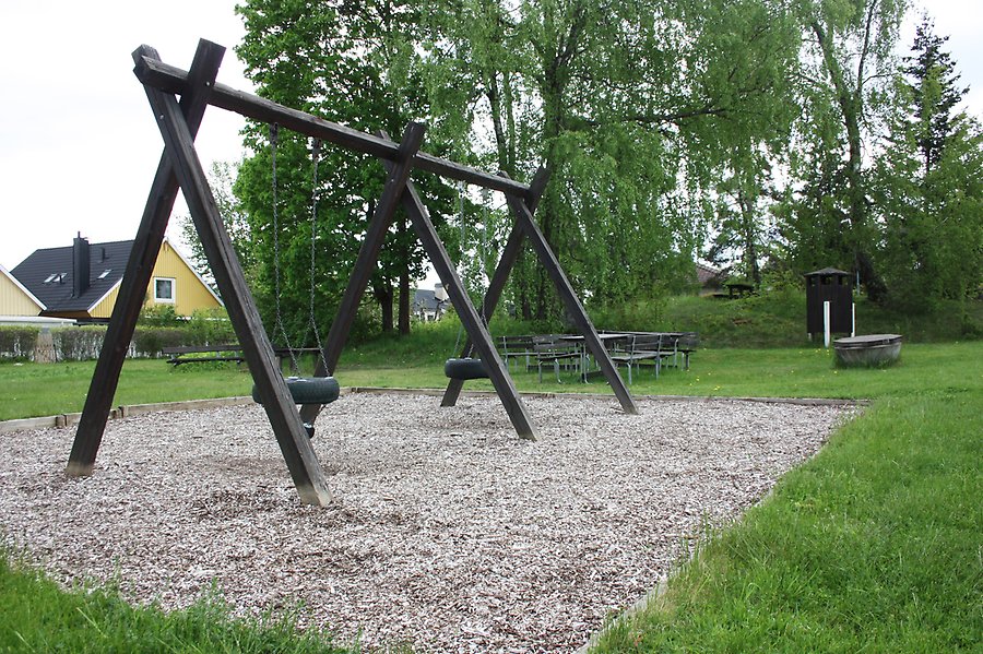 Lekplats med gungställning och bänkar med bord intill en skogsdunge.